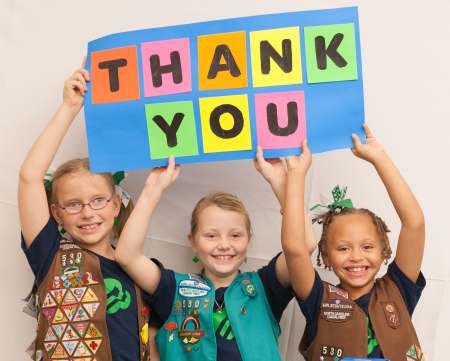 3 young girls in Girl Scout vests holding a sign that reads, "THANK YOU"